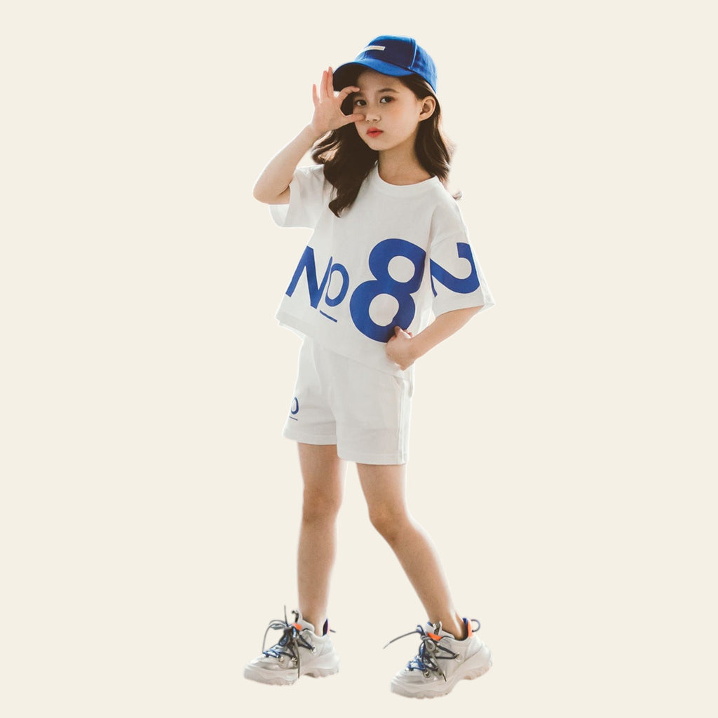 Child wearing a white t-shirt with blue text and shorts, standing on a textured floor.