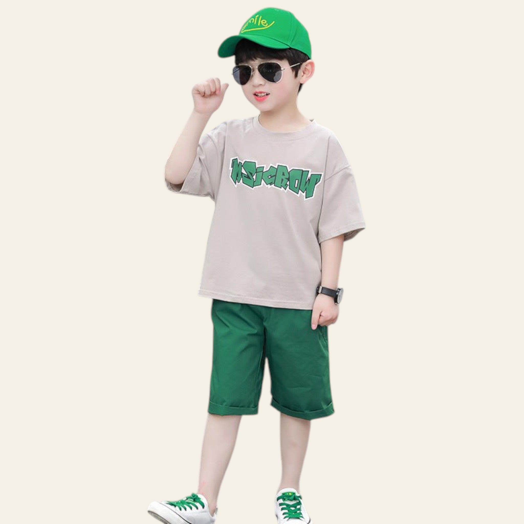 Child wearing a beige shirt with green text, green shorts, and a green cap on a street.