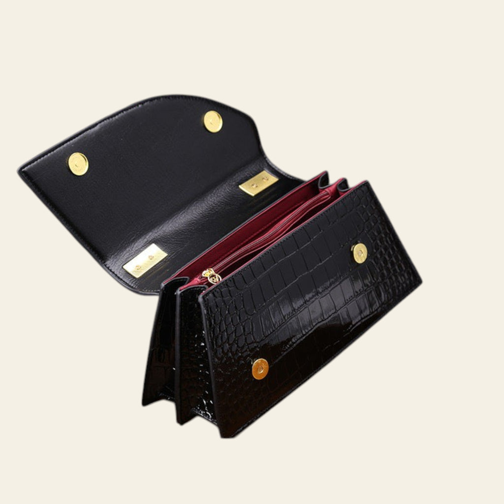 Black crocodile-patterned wallet with gold accents on a wooden surface.