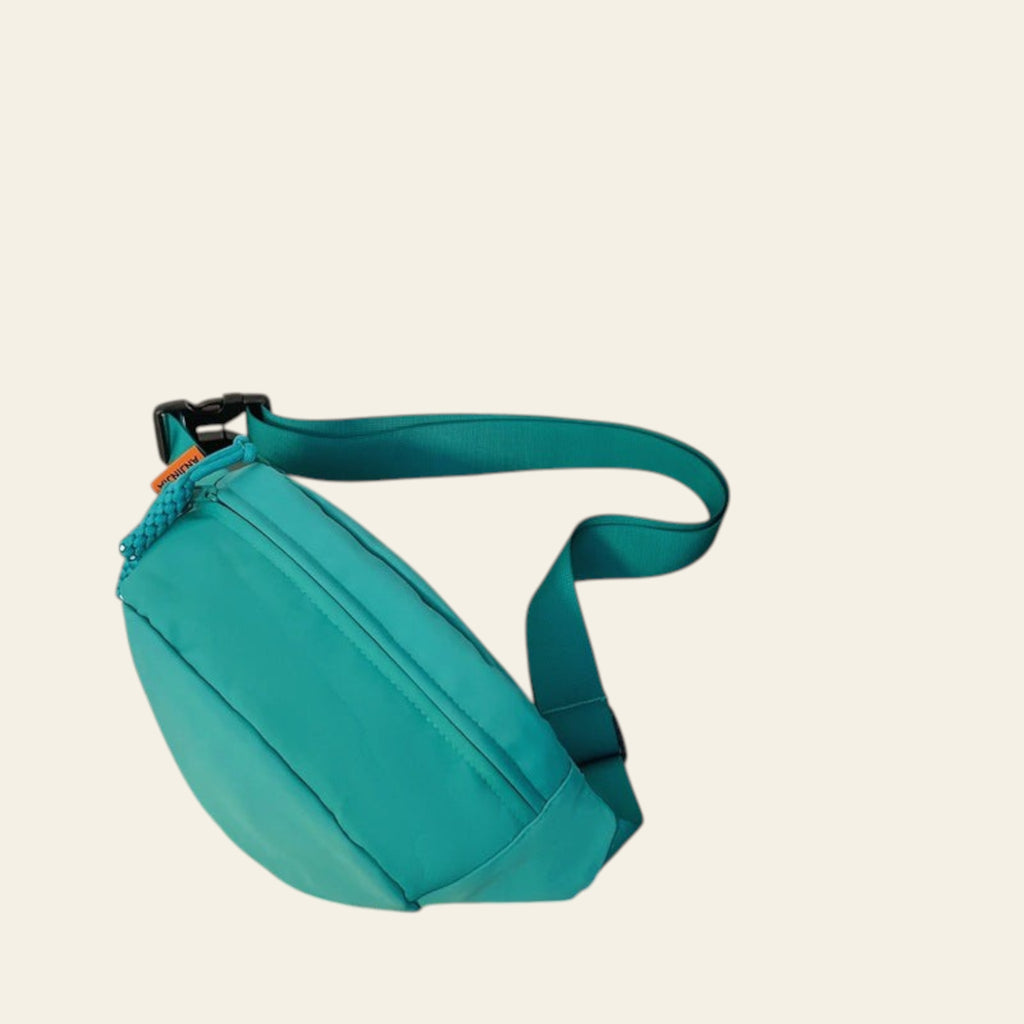 Turquoise waist bag on a glass surface with books and a wooden item in the background