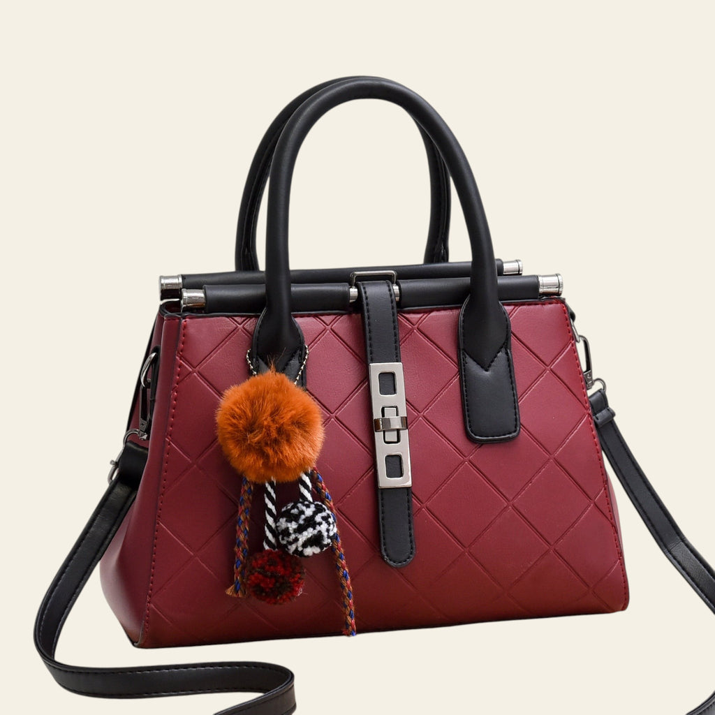 Red handbag with black handles and trim, featuring a decorative pom-pom charm on a white background.
