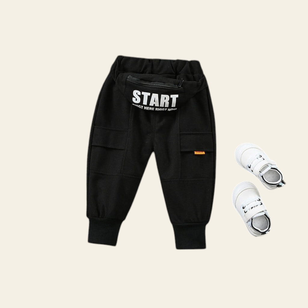 Black cargo pants with 'START' text and white sneakers on a textured gray surface.