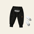 Black cargo pants with 'START' text and white sneakers on a textured gray surface.