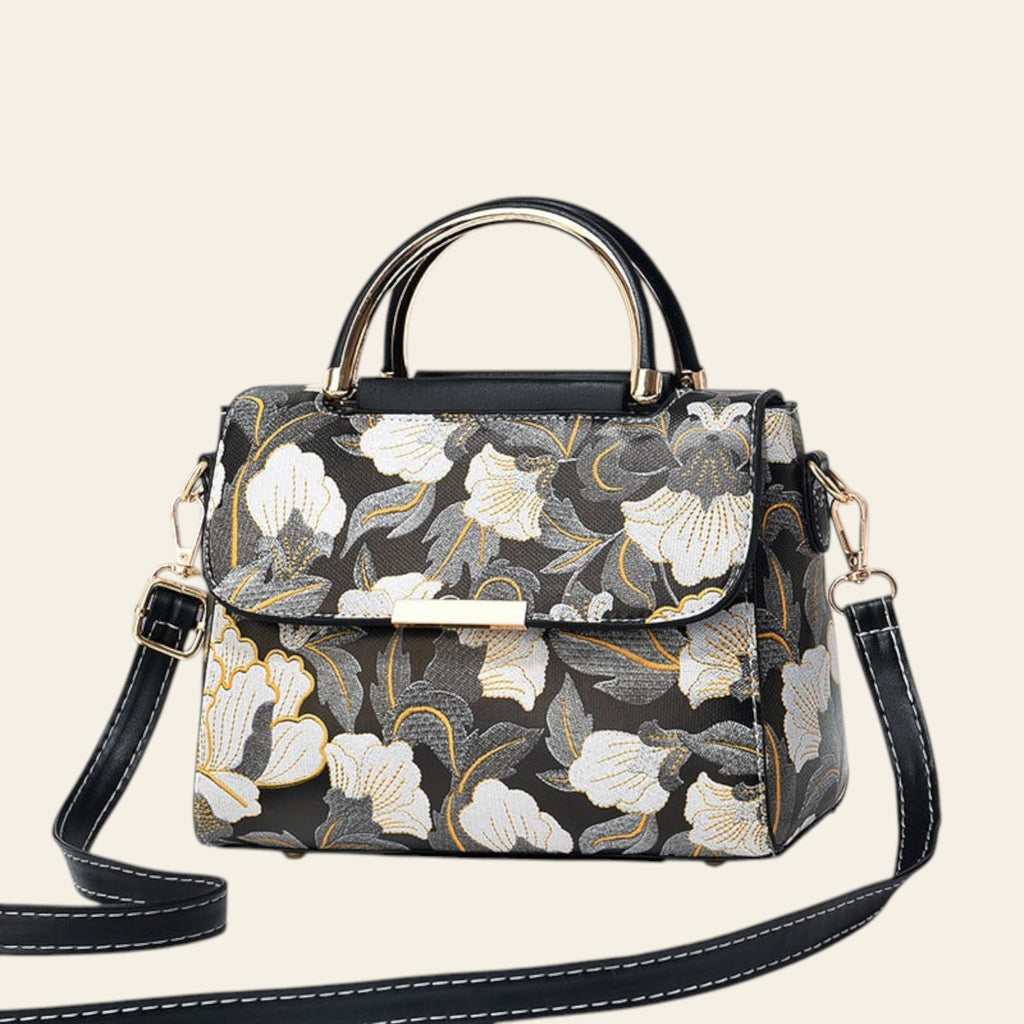 Floral patterned handbag with a black strap on a white surface.