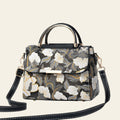 Floral patterned handbag with a black strap on a white surface.