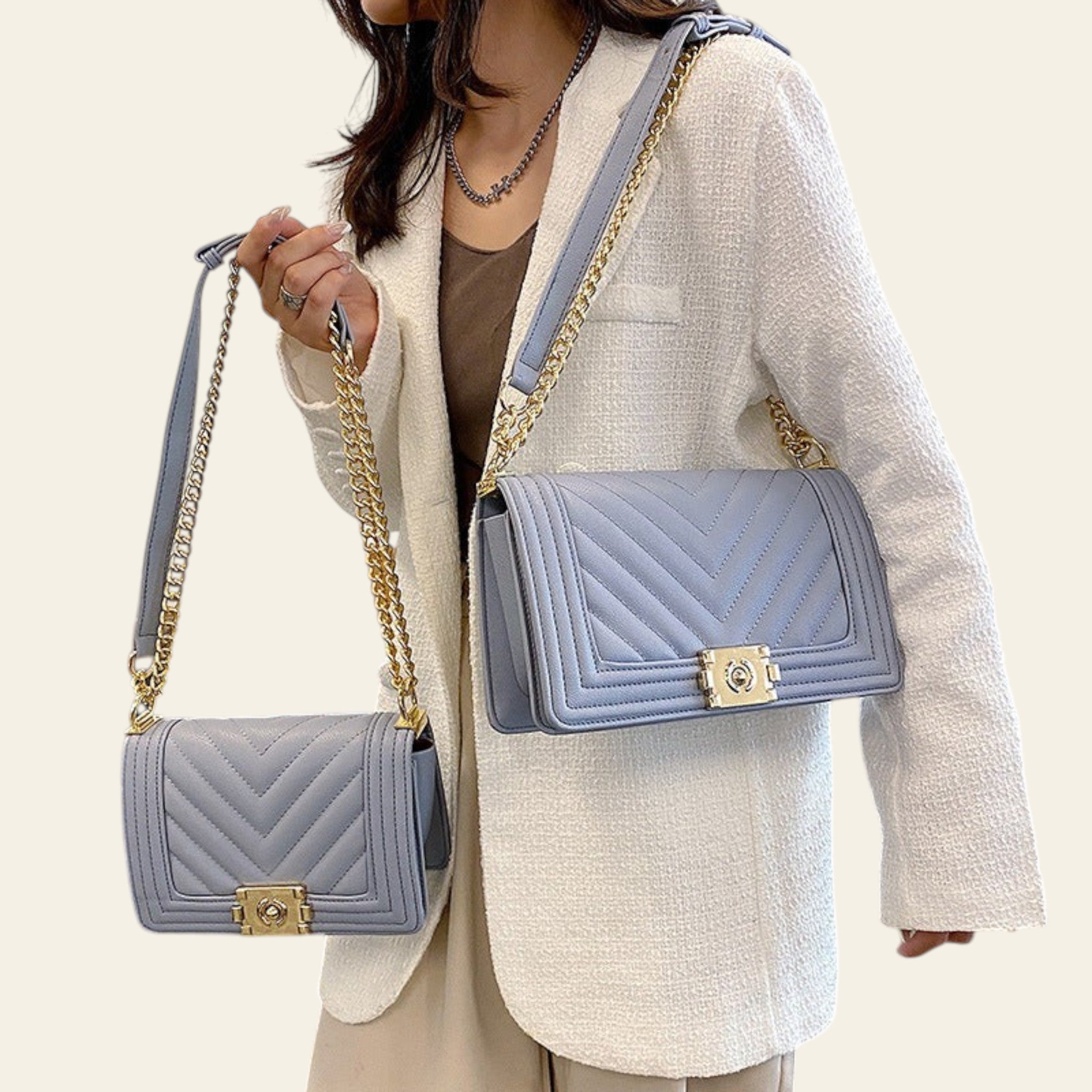 Person holding two blue handbags with gold chains in an indoor setting