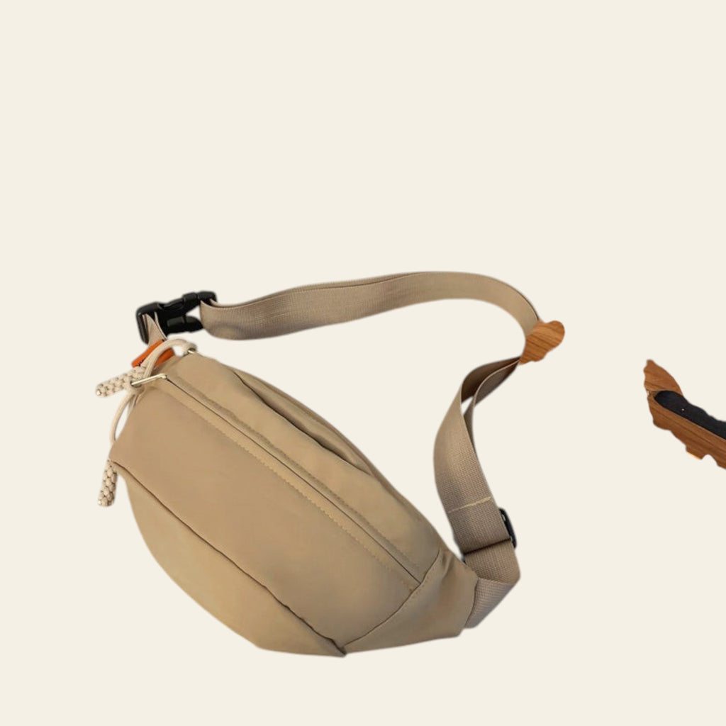 Beige waist bag on a glass surface with a book and snack packet in the background