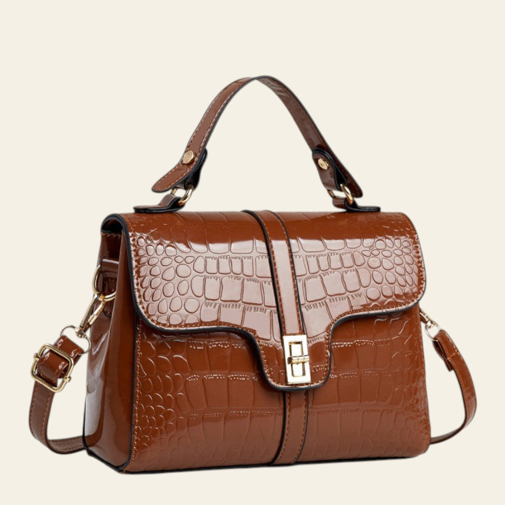Brown crocodile-patterned handbag on a light surface with a neutral background