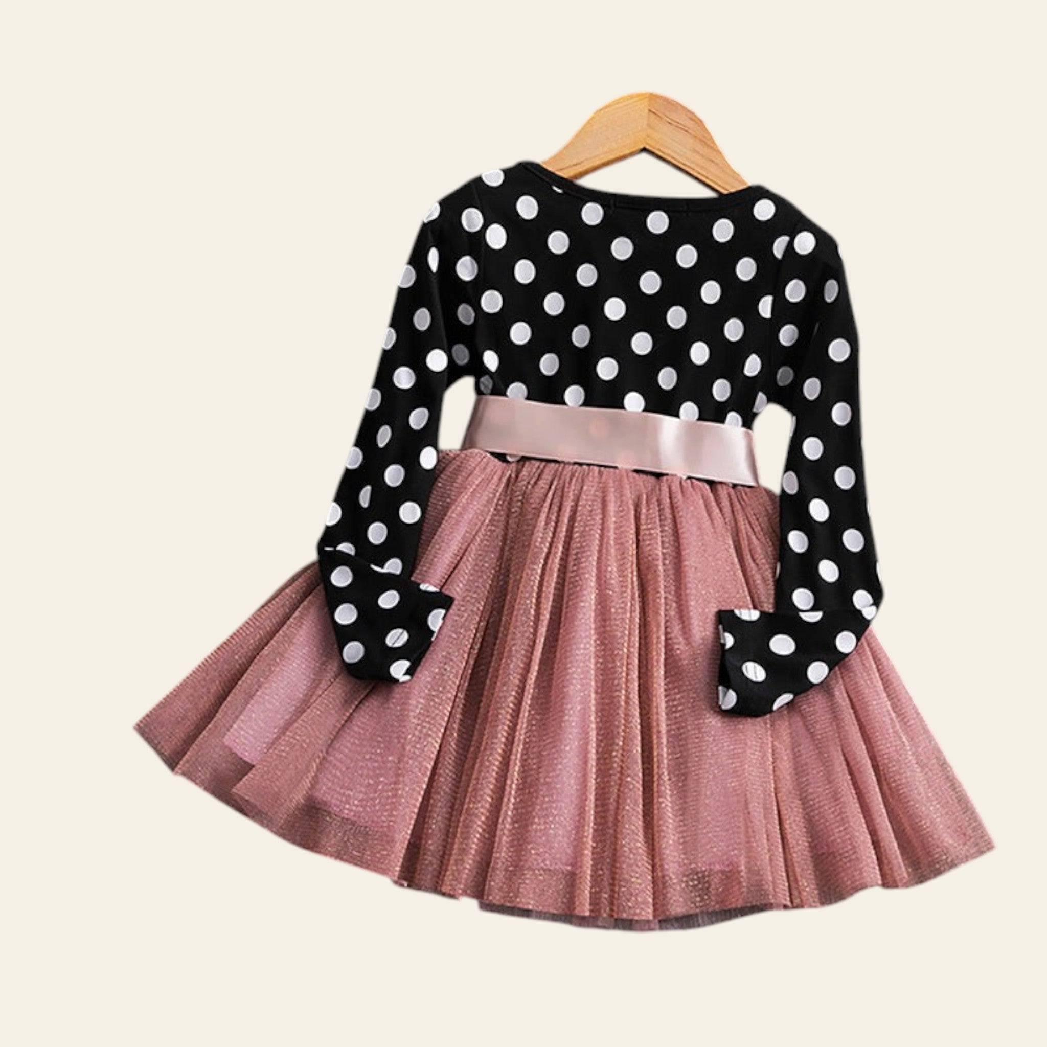 Black polka dot long-sleeve top with pink pleated skirt on a wooden surface.