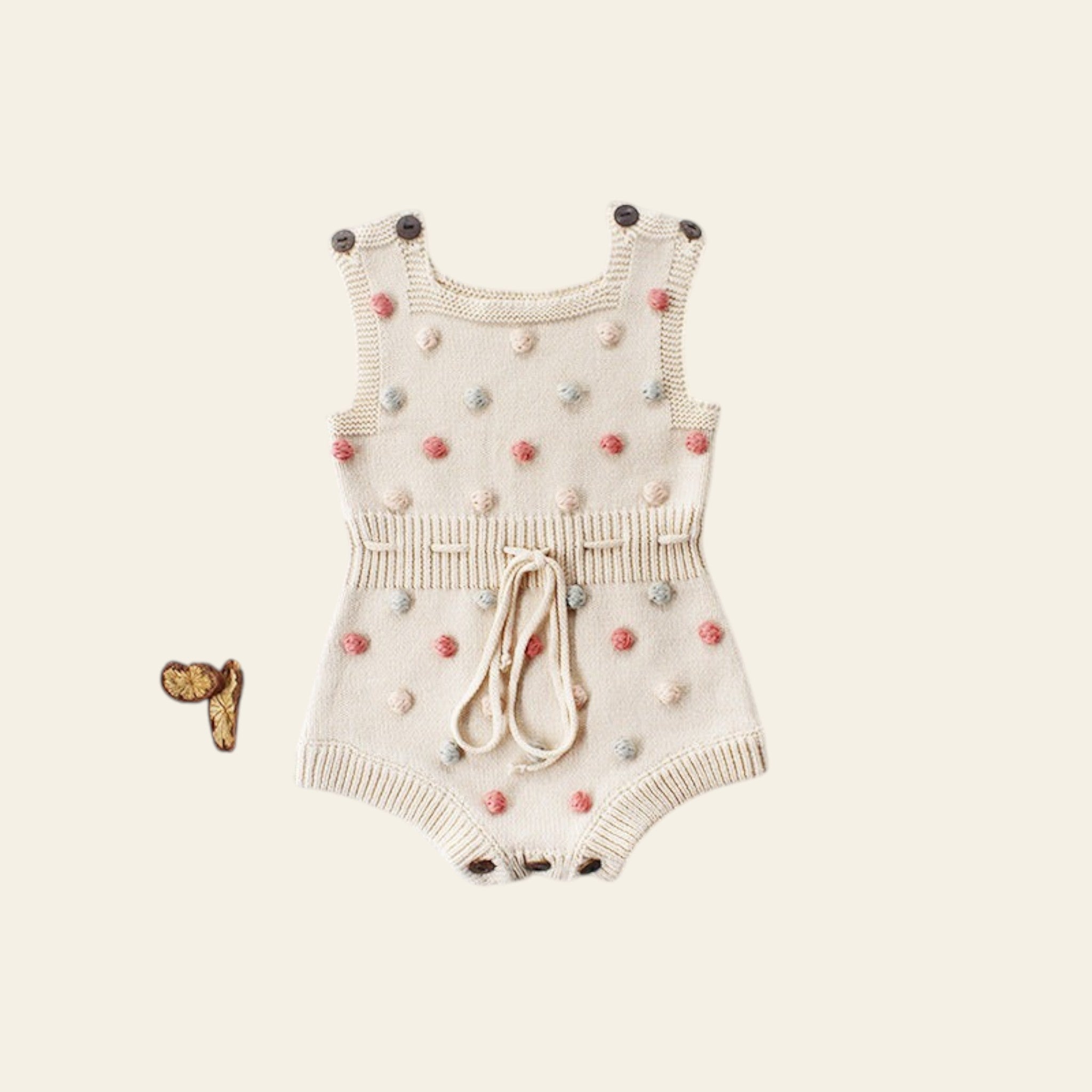Baby romper with pom-pom details on a light gray background