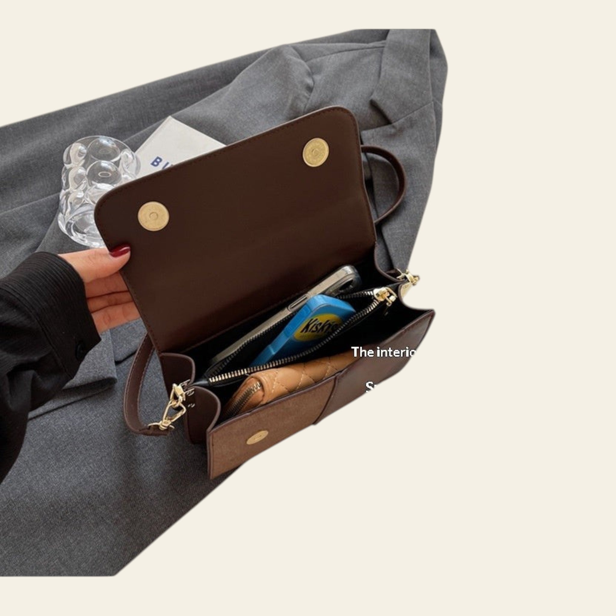 Brown clutch bag with gold accents held open to show interior space on a gray surface.