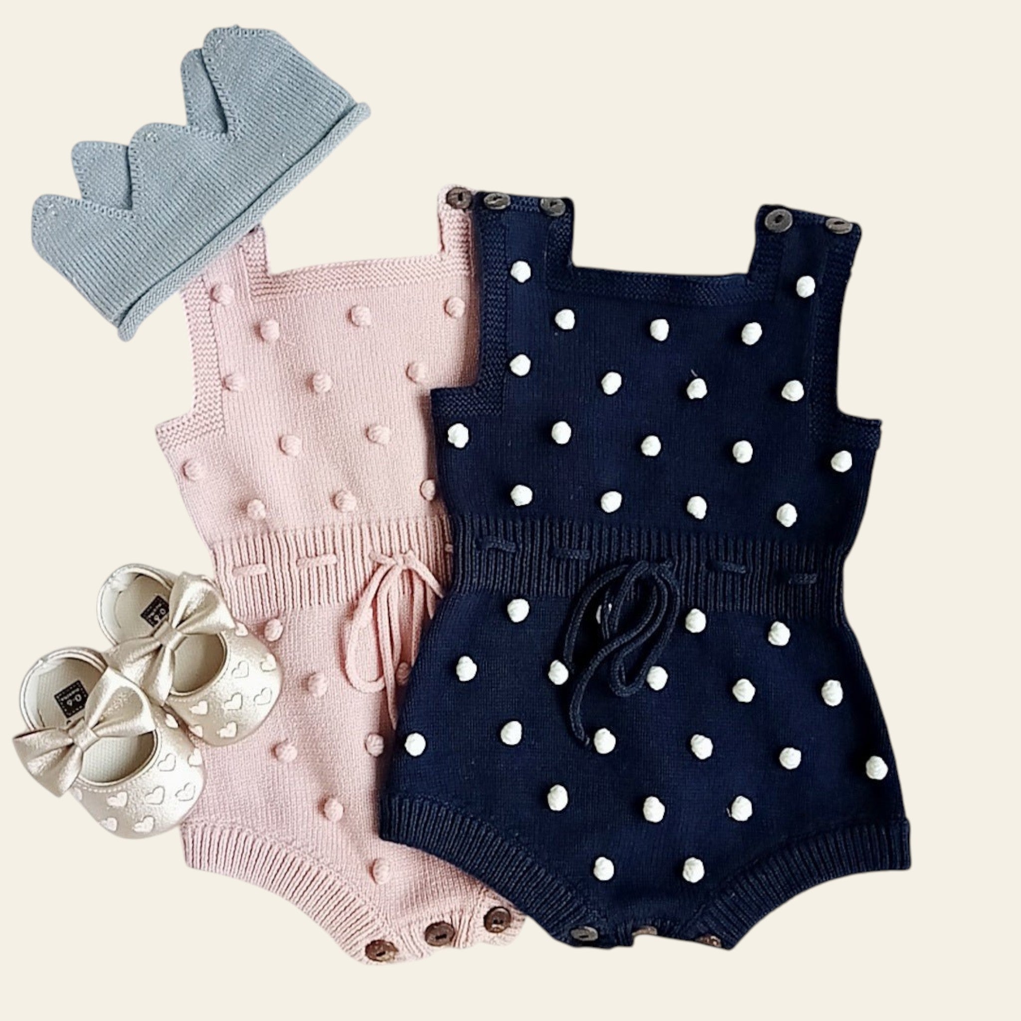 Two baby rompers, a hat, and shoes on a white surface