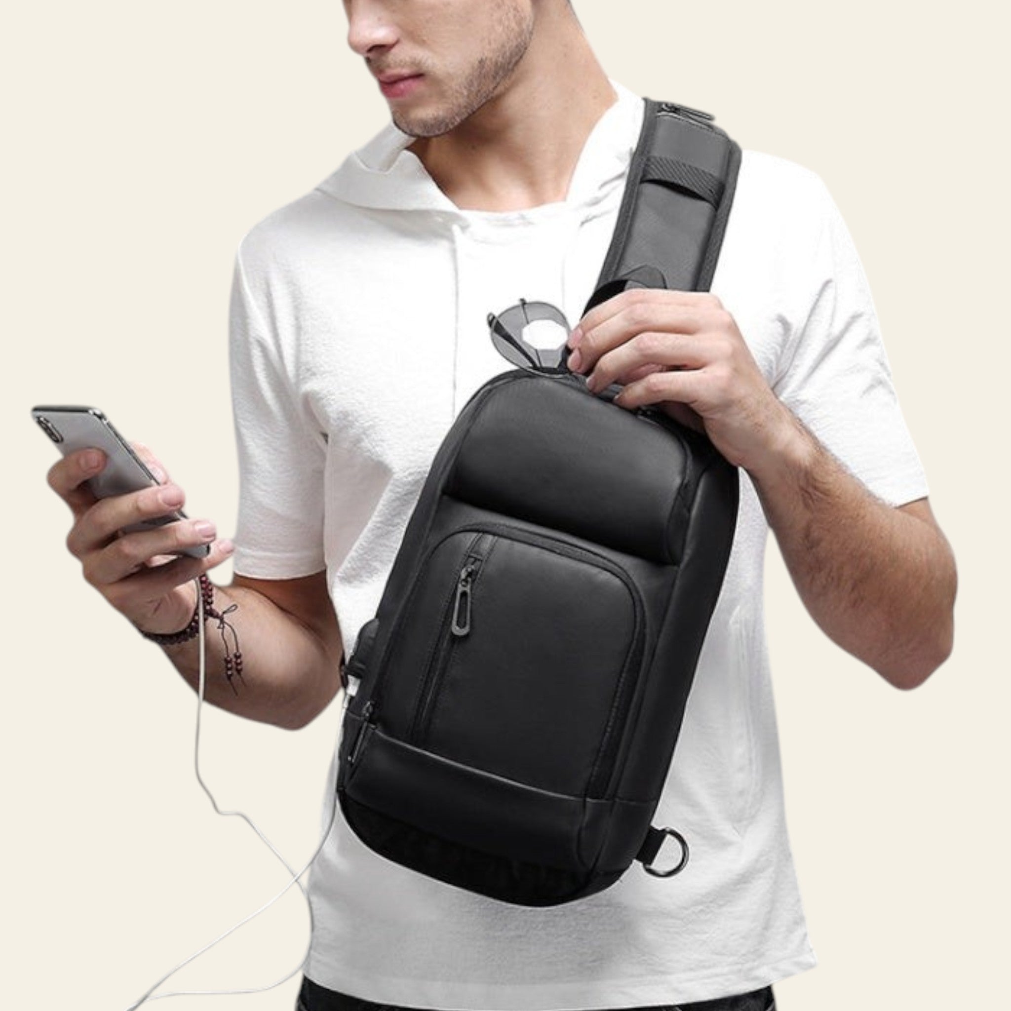 Man holding a black crossbody bag and a smartphone on a gray background