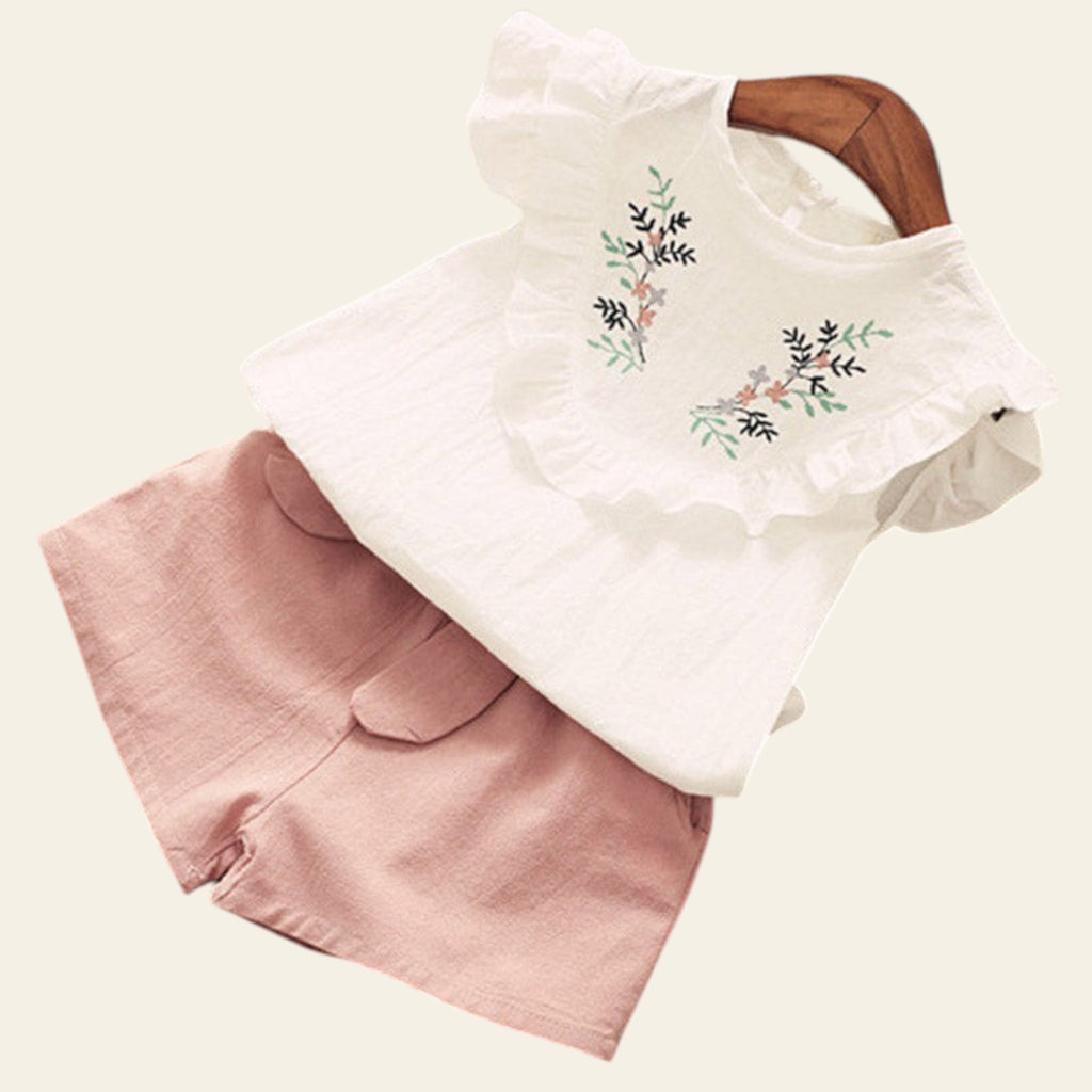 White blouse with floral embroidery and pink shorts on a wooden surface