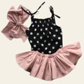 Black polka dot top with pink ruffled skirt and matching bow on a fluffy white surface