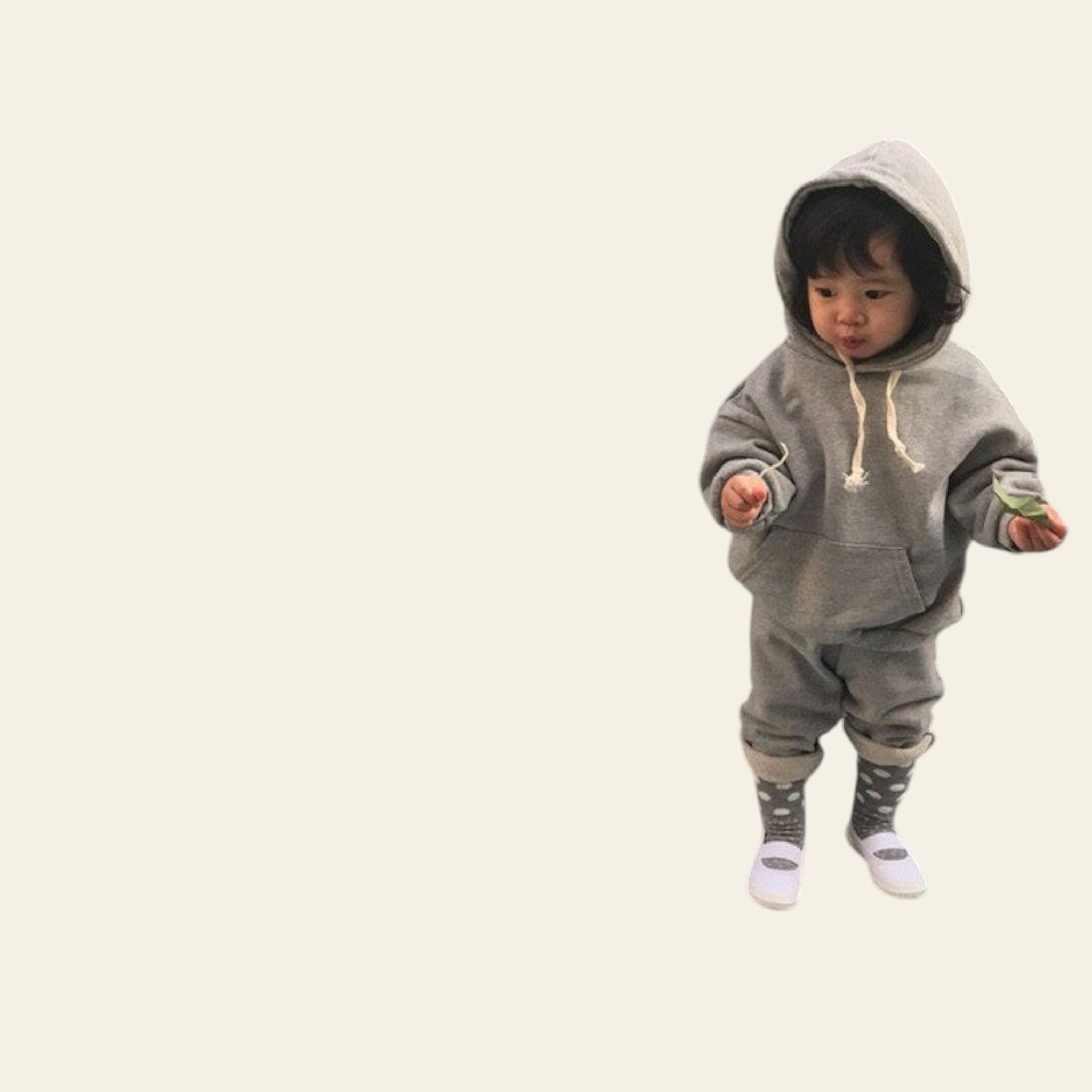 Child wearing a gray hoodie and pants standing against a plain wall.
