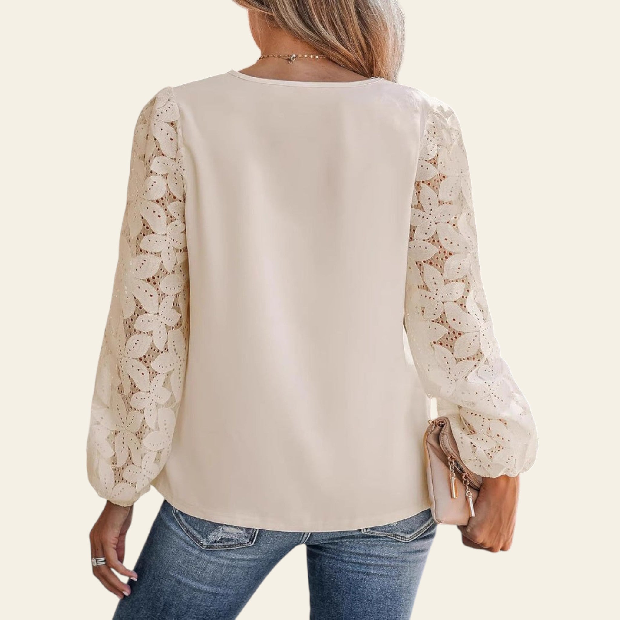Woman wearing a cream blouse with lace sleeves and blue jeans, holding a beige clutch.