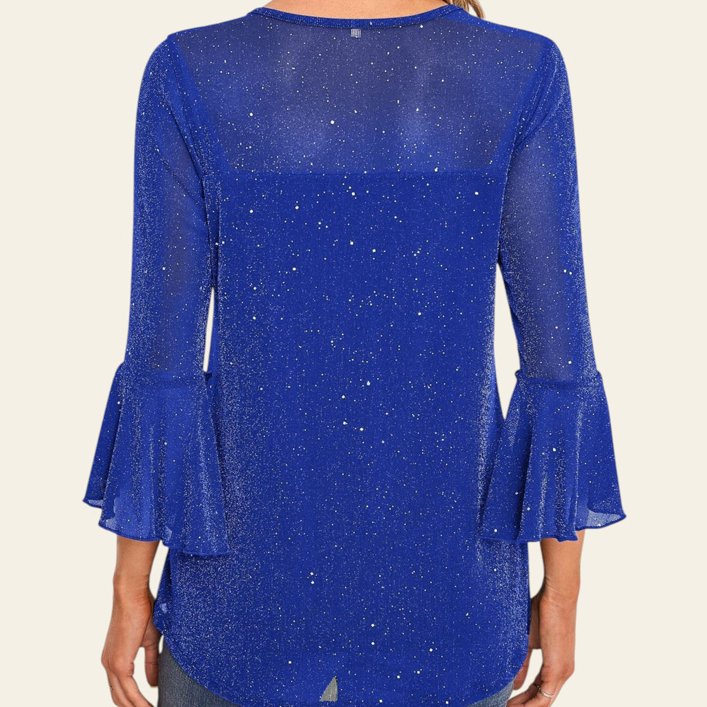 Blue blouse with ruffled sleeves worn by a person, against a decorative wall.