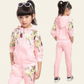 Young girl wearing a pink tracksuit with floral patterns in a room.