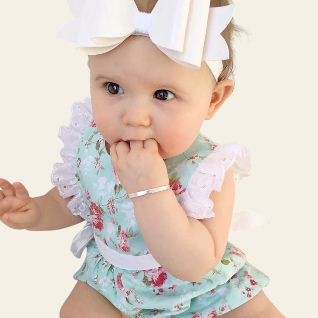 Baby wearing a floral romper with ruffles and a large white bow.
