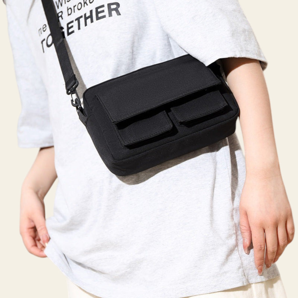 Person wearing a black crossbody bag with a plain background