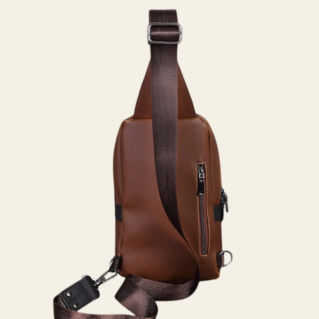 Brown leather sling bag on a dark wooden surface with a grid-patterned wall in the background.