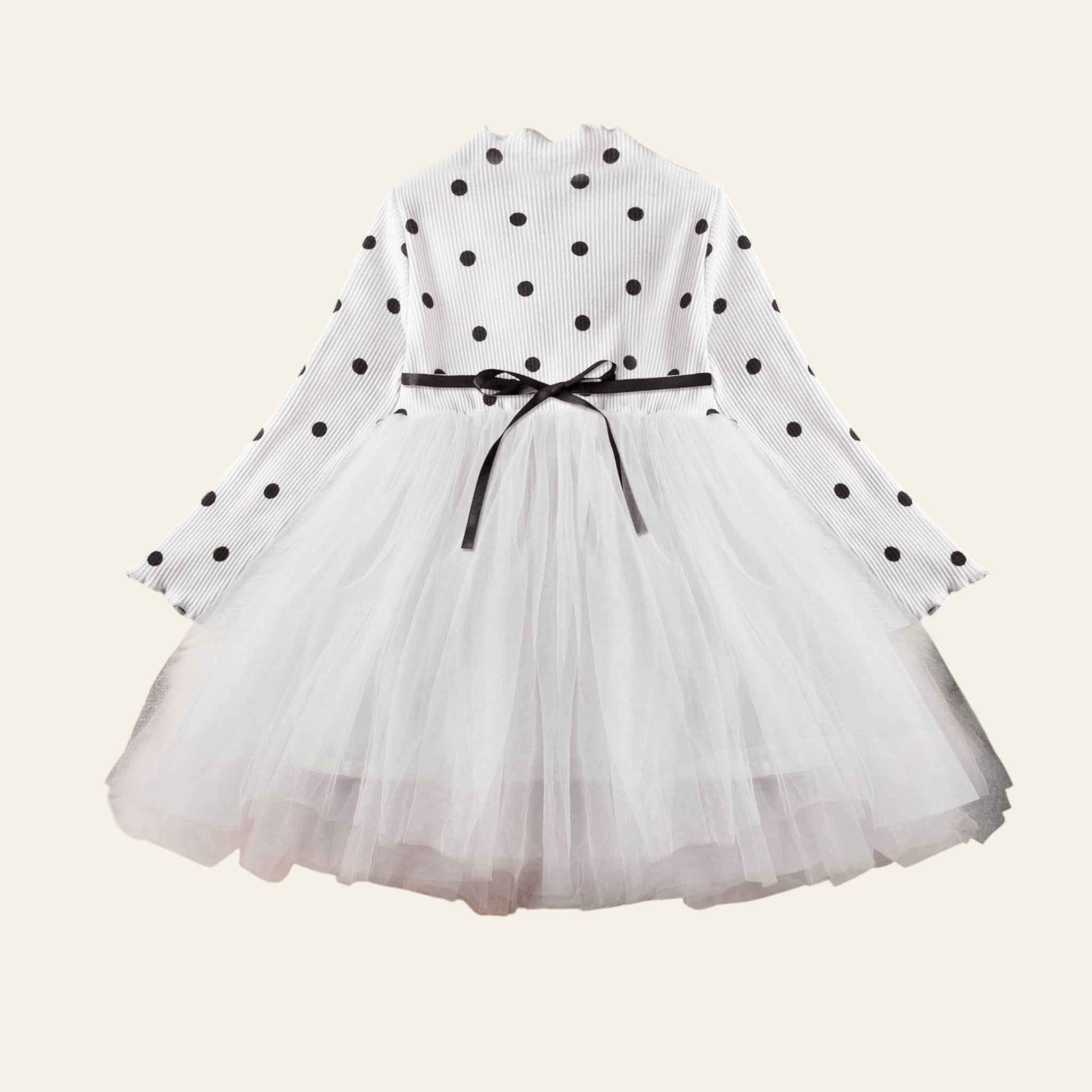 White dress with black polka dots and a black ribbon on a fluffy white surface.