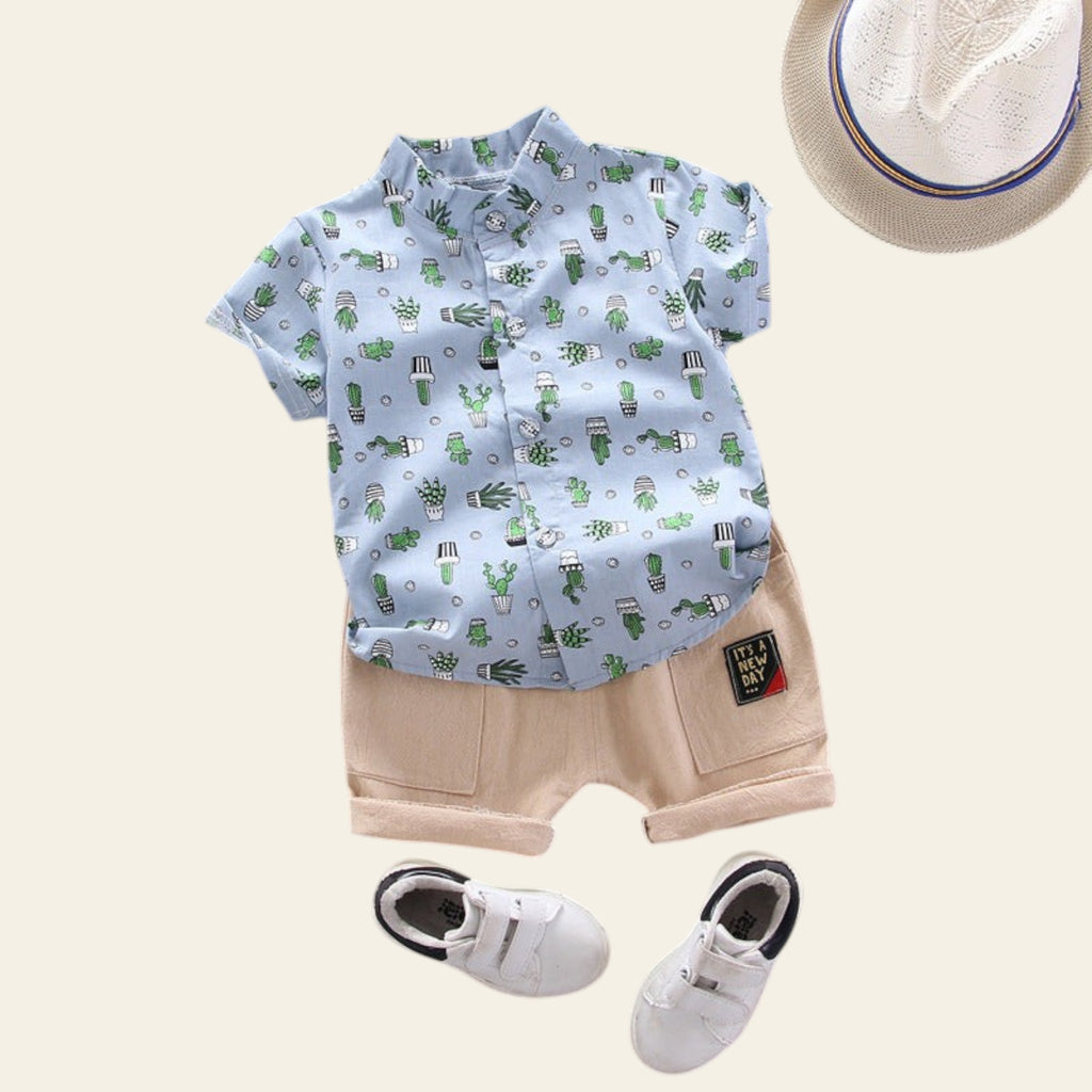 Children's outfit with cactus-patterned shirt, beige shorts, white sneakers, and a hat on a gray background.