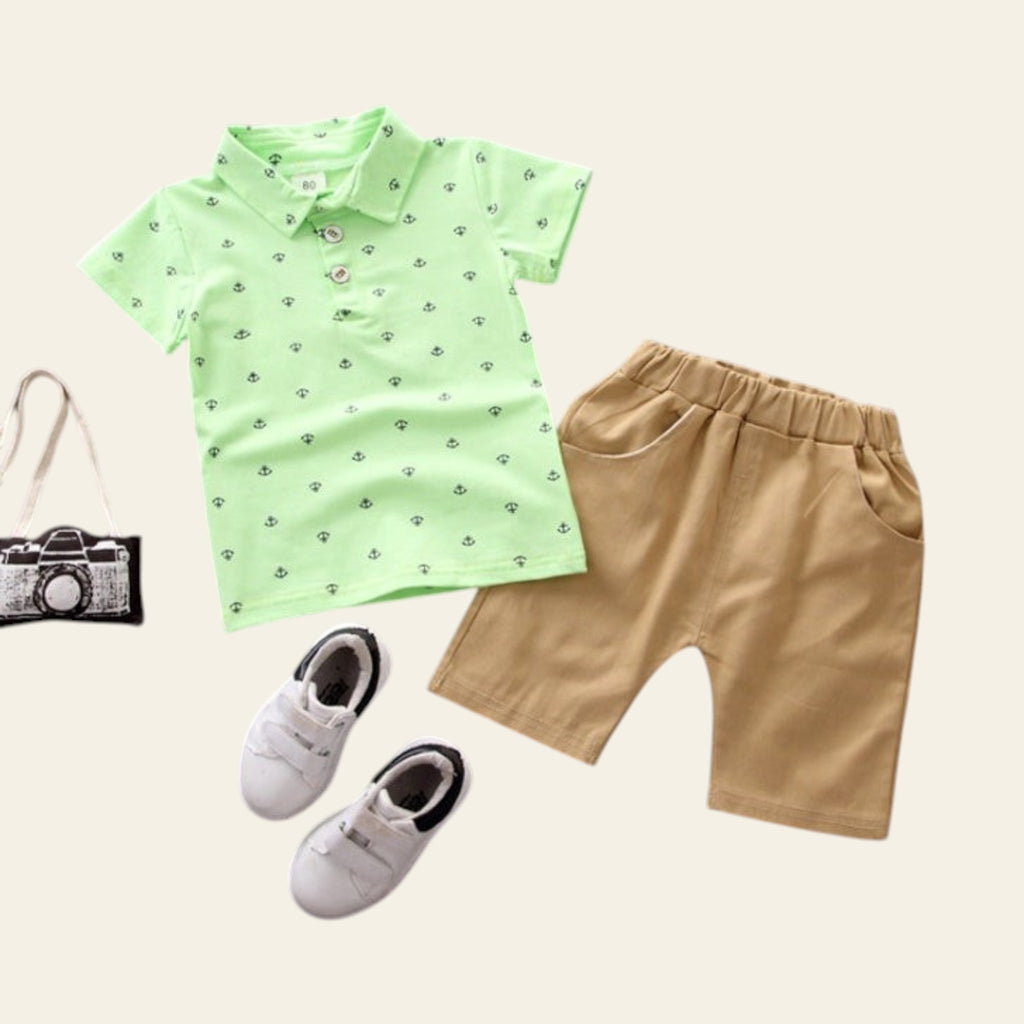Children's green shirt with black patterns, beige shorts, white shoes, and a small camera on a gray background
