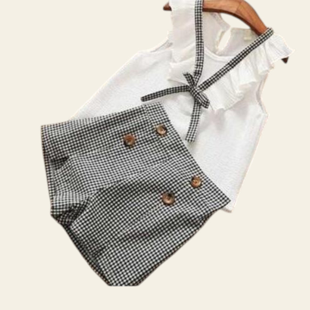 White sleeveless top with ruffled details and plaid shorts on a wooden surface.