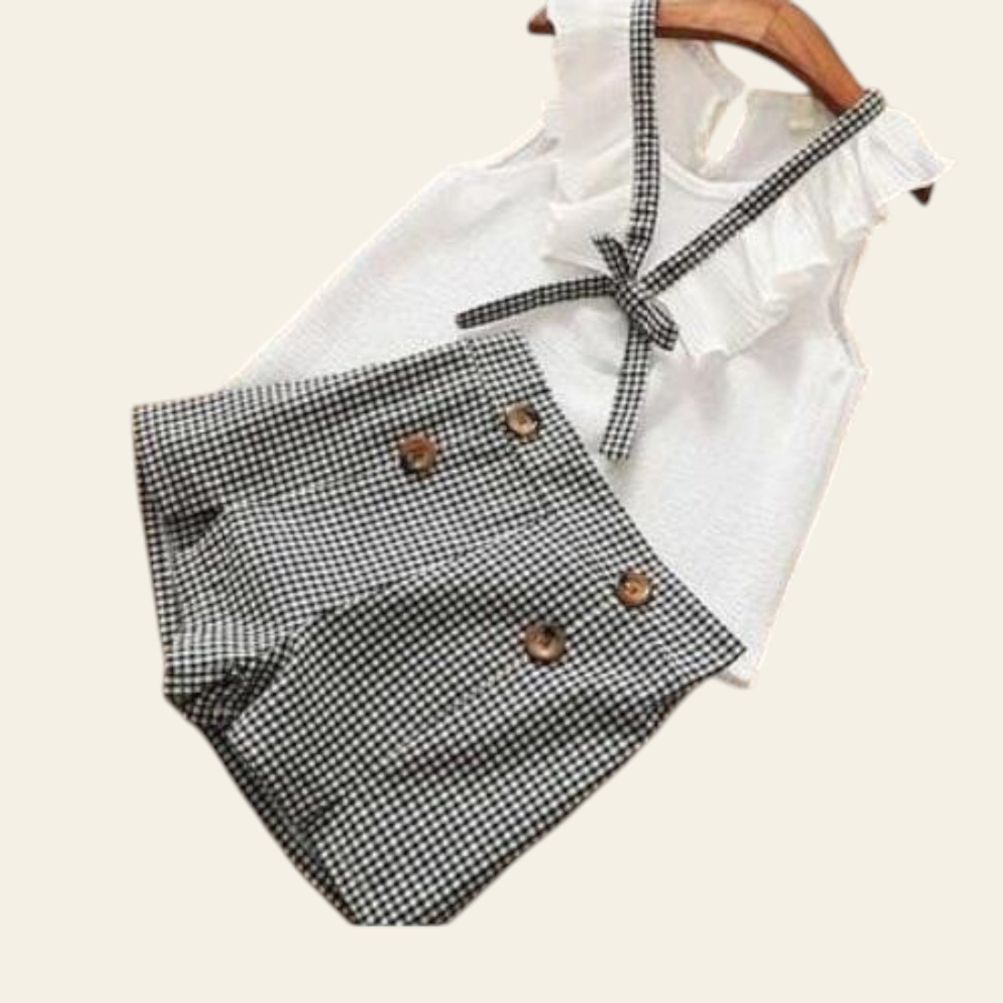White sleeveless top with ruffled details and plaid shorts on a wooden surface.