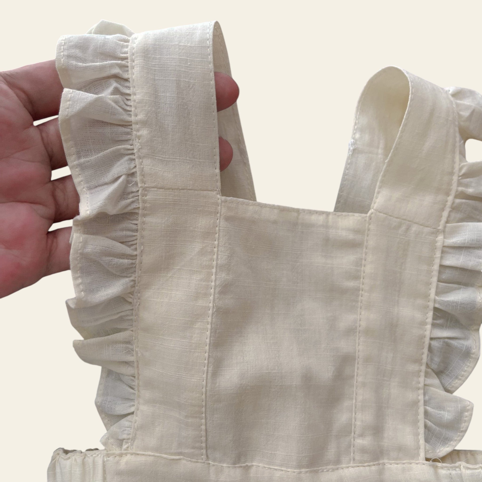 Beige tote bag with ruffled handles held by a person wearing a green checkered shirt.