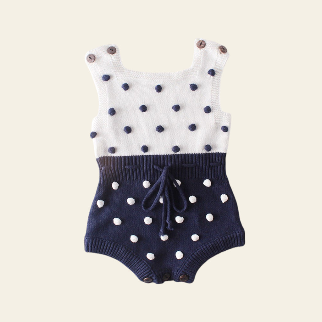 Baby romper with white and navy polka dot pattern on a light gray background