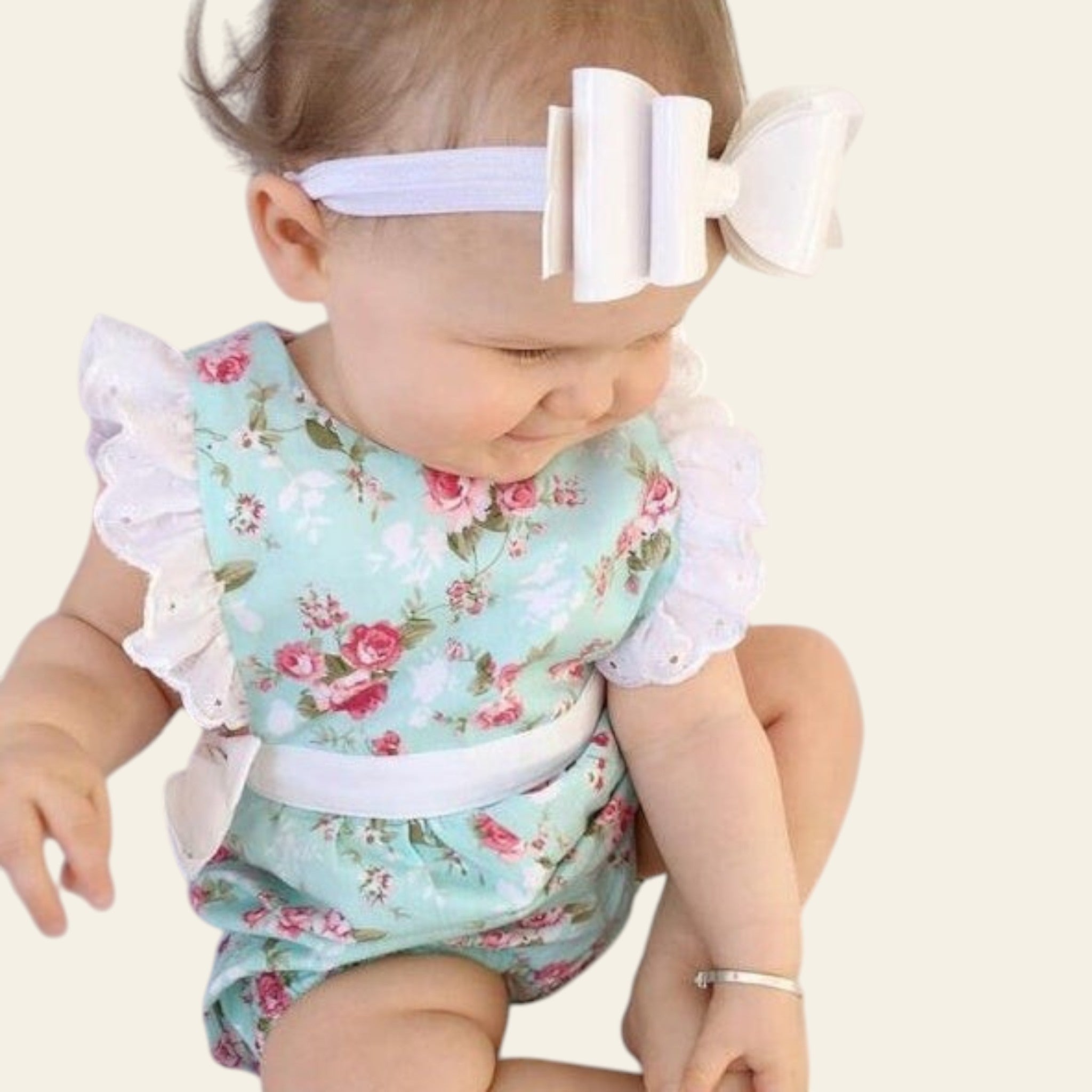 Baby wearing a floral romper with ruffles and a large white bow on a light background