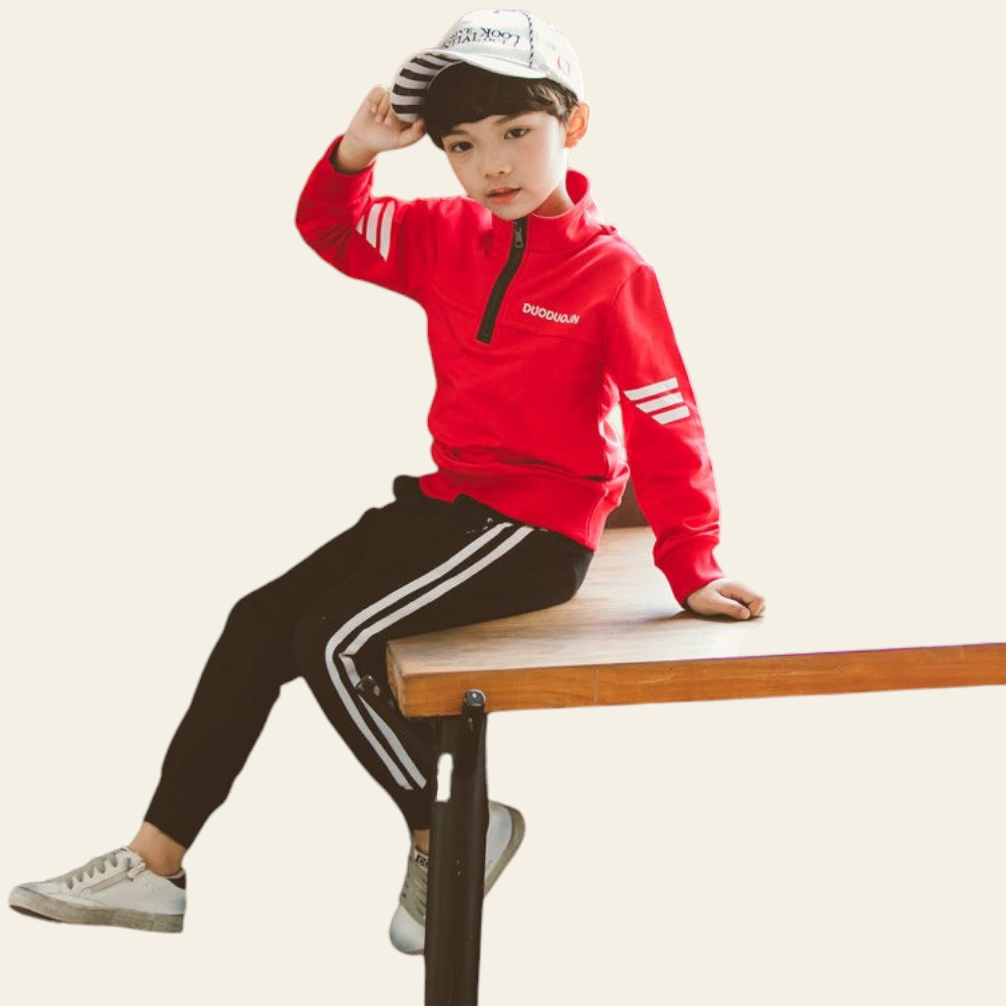 Child wearing a red jacket and black pants with white stripes, sitting on a wooden bench.