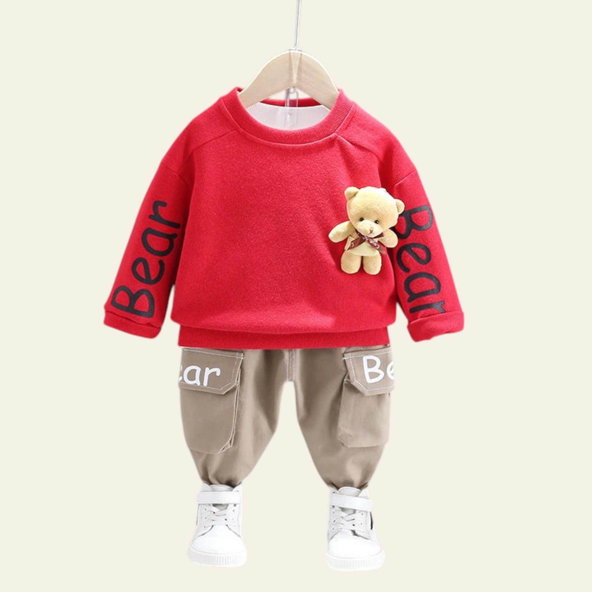Red sweater with teddy bear and 'Bear' text, beige pants, and white shoes on a gray background.
