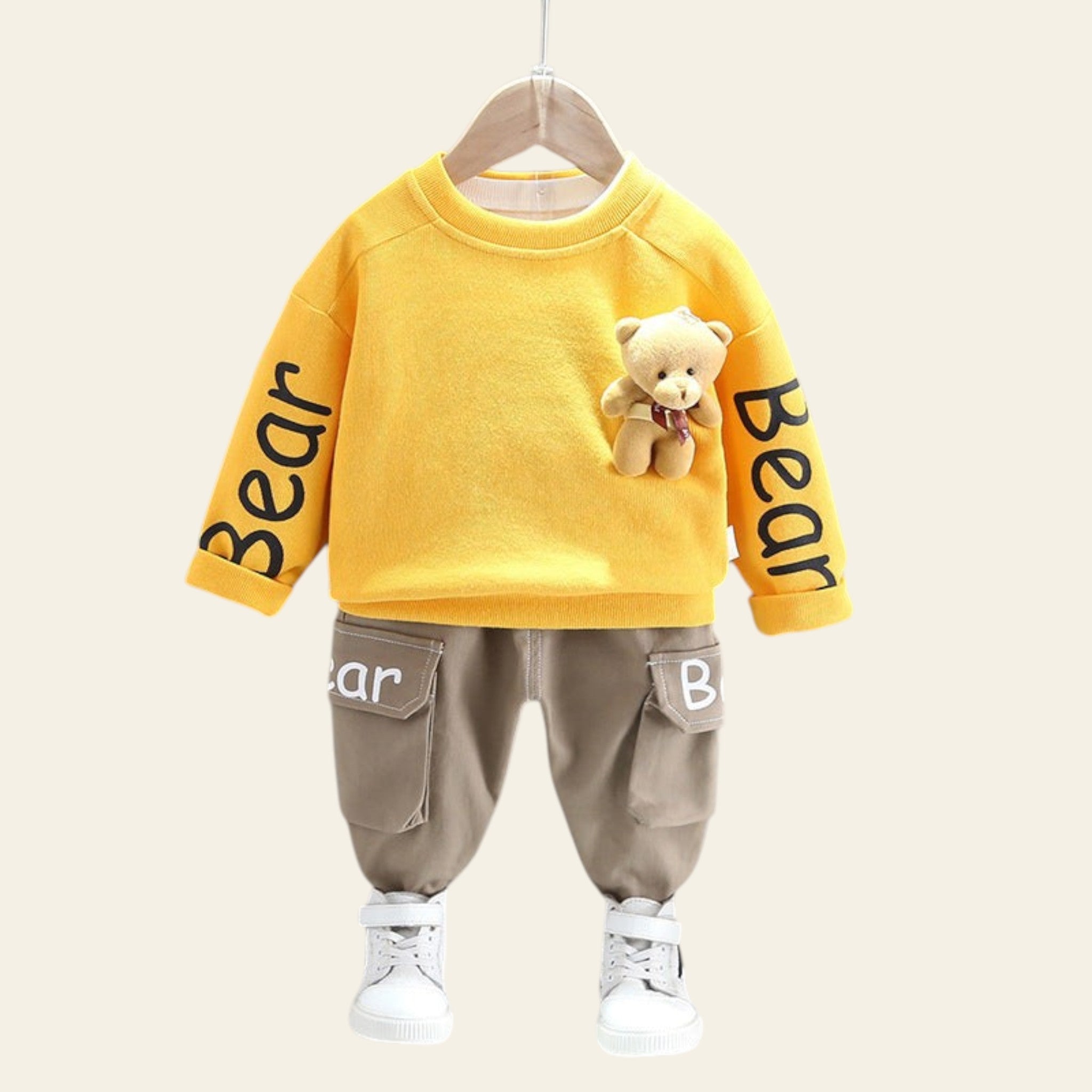 Children's outfit with yellow sweater and brown pants on a hanger against a gray wall.