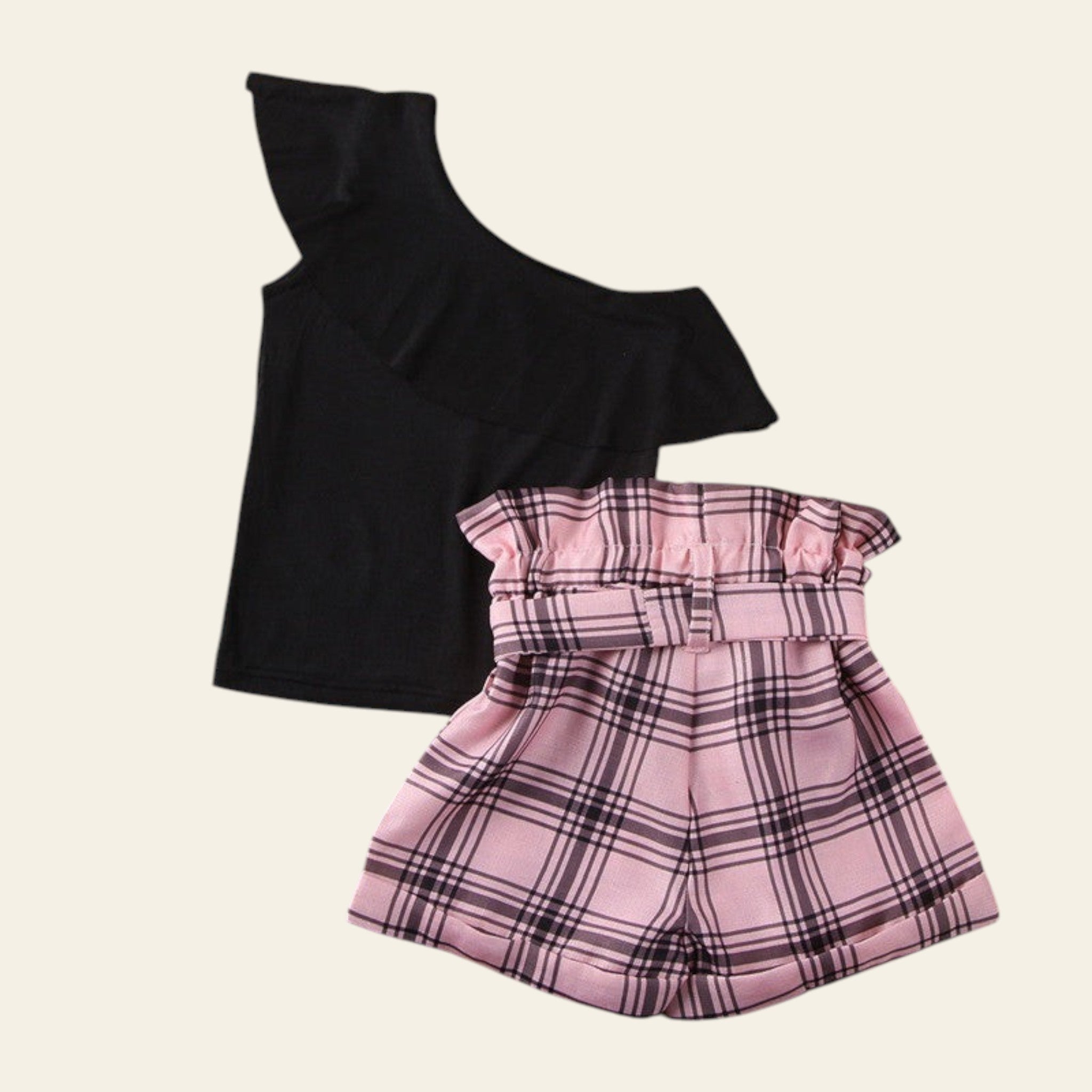 Black one-shoulder top and pink plaid shorts on a wooden surface.
