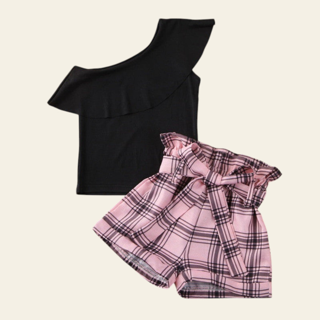 Black one-shoulder top and pink plaid skirt on a wooden surface