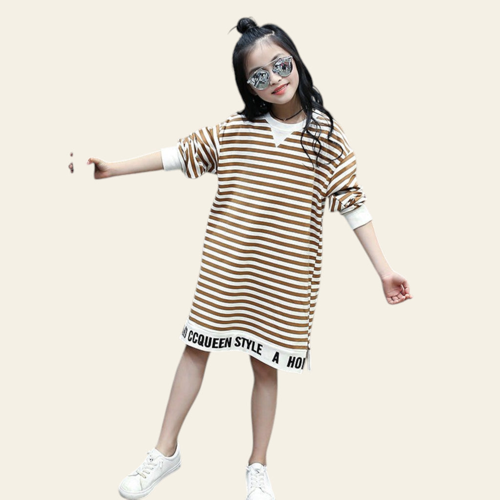 Young girl wearing a striped dress with text, standing outdoors near a cactus plant.