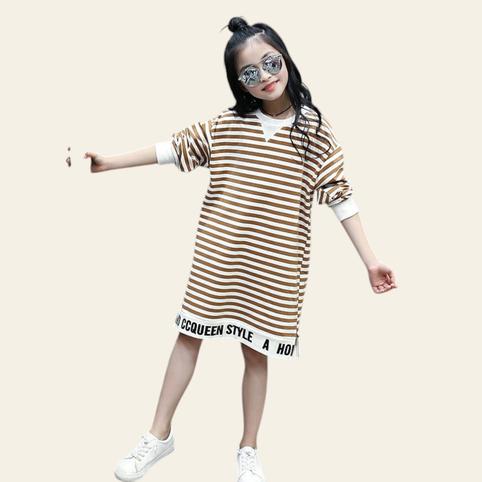 Young girl wearing a striped dress with text, standing outdoors near a cactus plant.