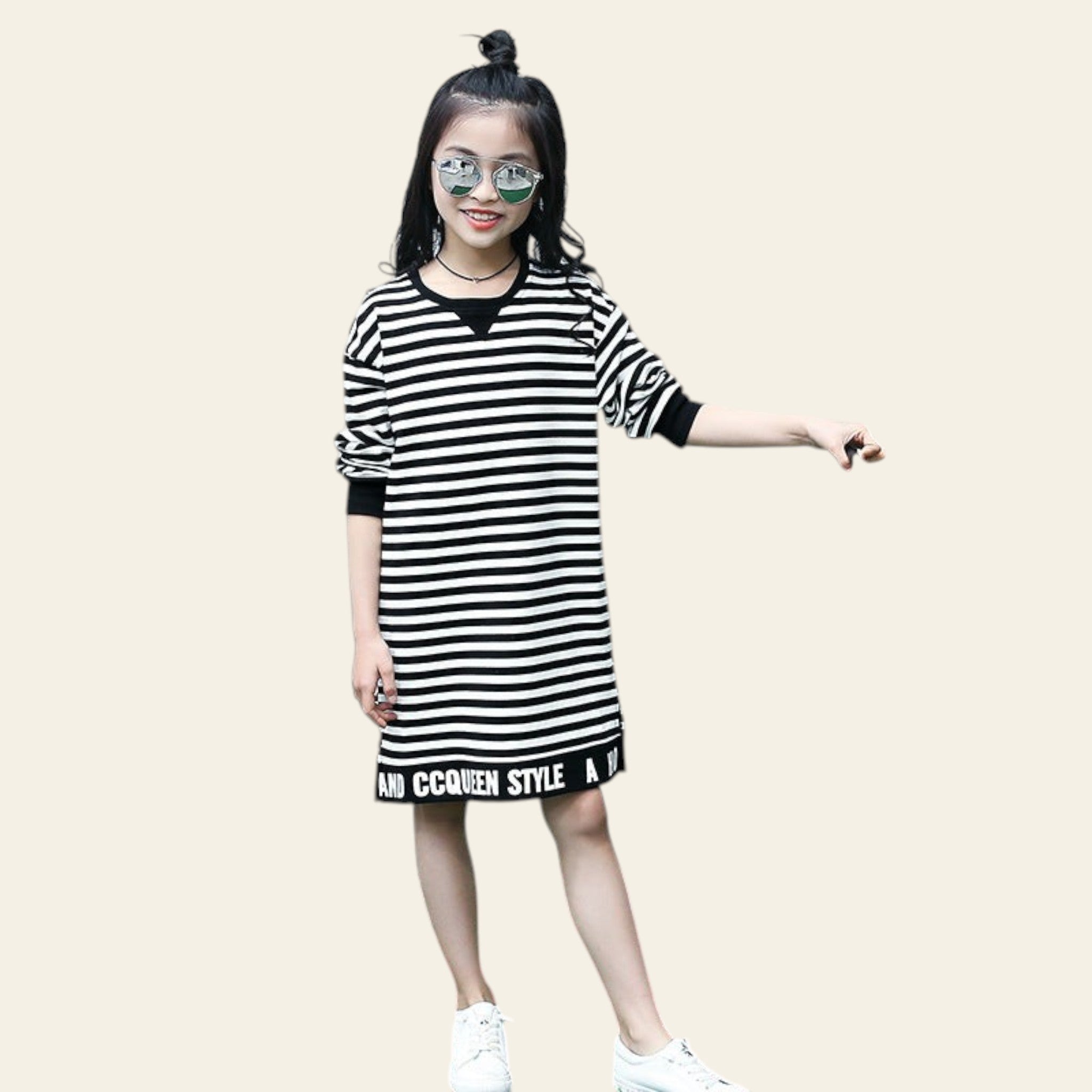 Young girl wearing a black and white striped dress with text, standing on grass next to a chair.
