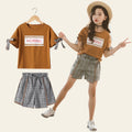 Woman wearing a matching outfit with a 'MORING' t-shirt and plaid shorts, standing next to the outfit on a hanger.