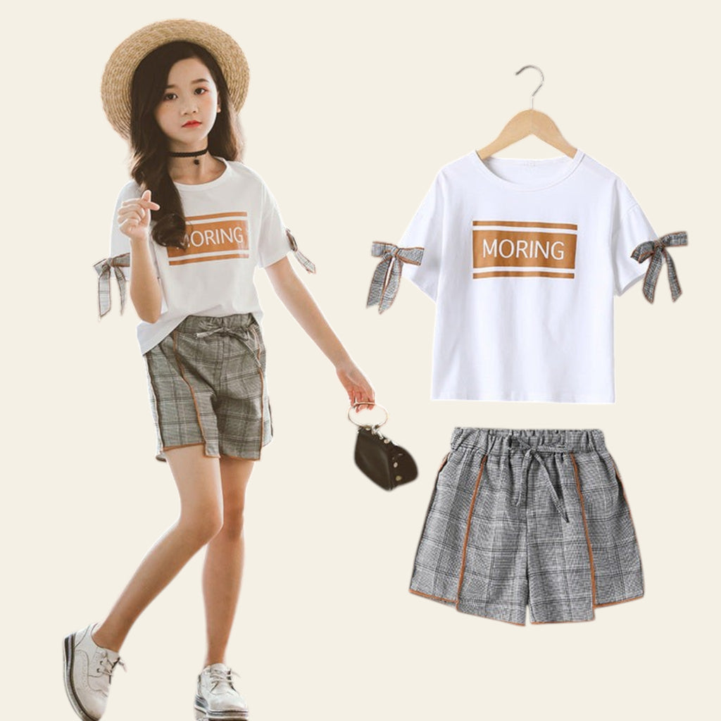 Woman wearing a white t-shirt with 'MORING' text and plaid shorts, standing next to the clothing items.