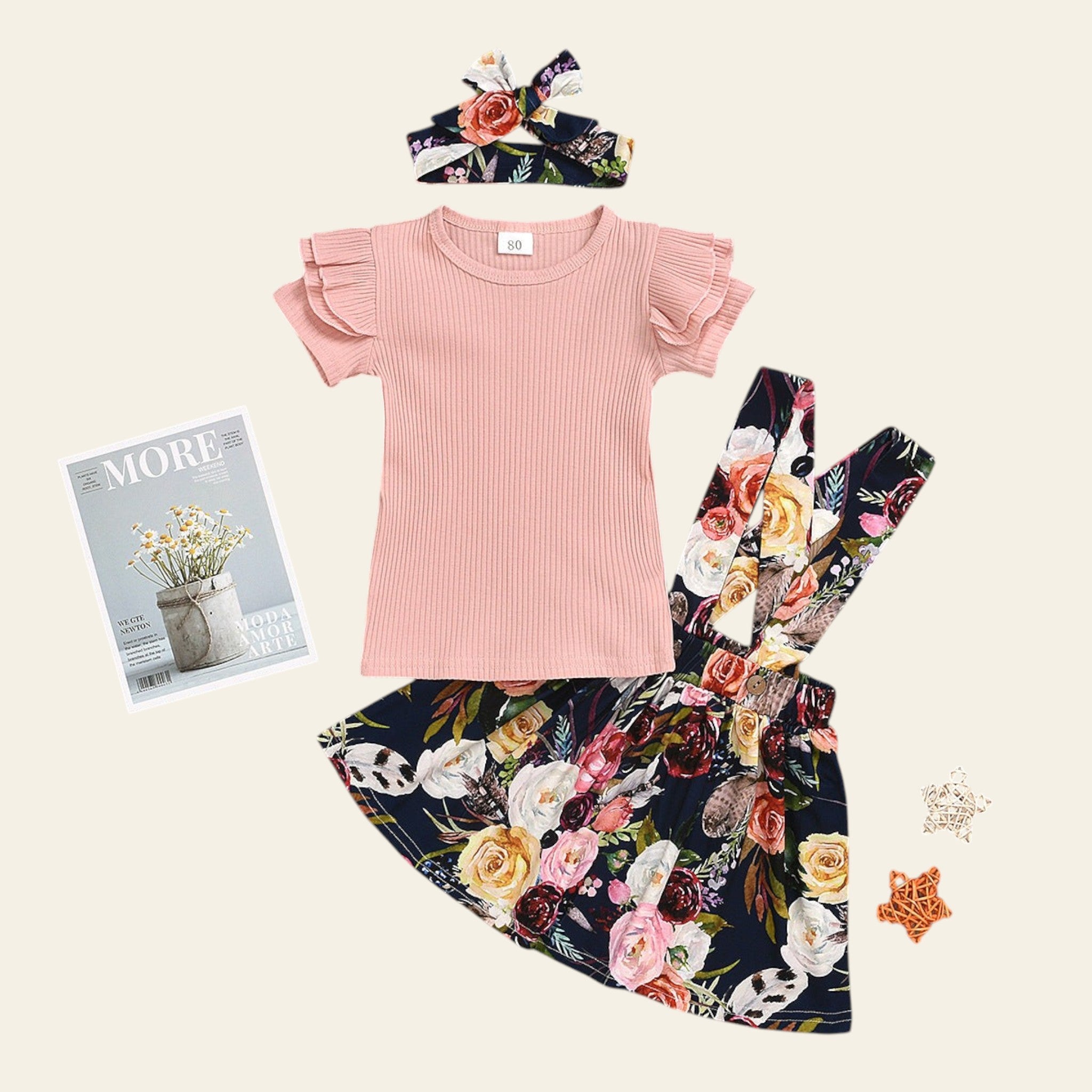 Pink ruffled top and floral skirt set on a wooden surface with a magazine and decorative items.