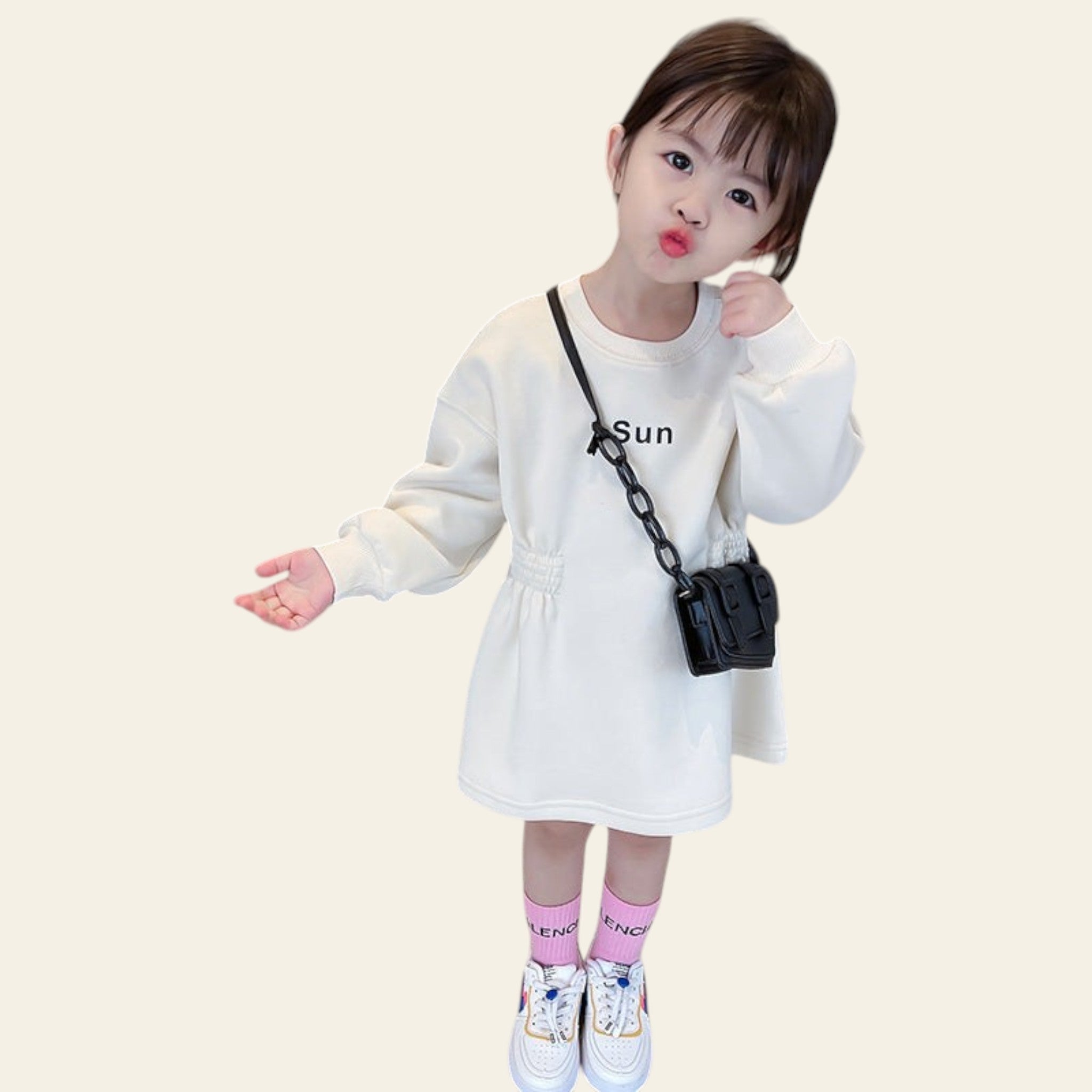 Child wearing a white dress with a small black bag, standing indoors.