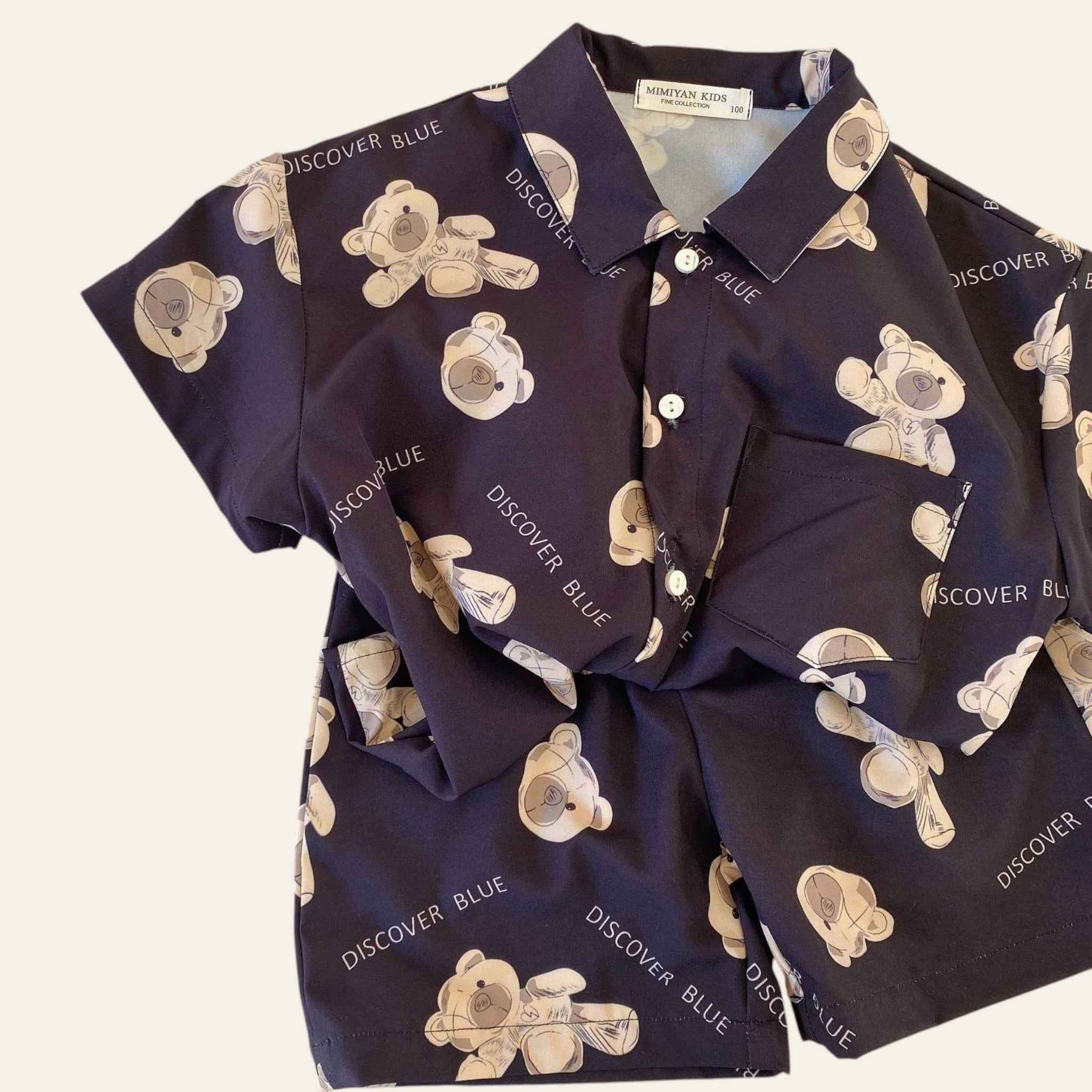 Navy shirt with teddy bear pattern and 'DISCOVER BLUE' text on a beige surface.