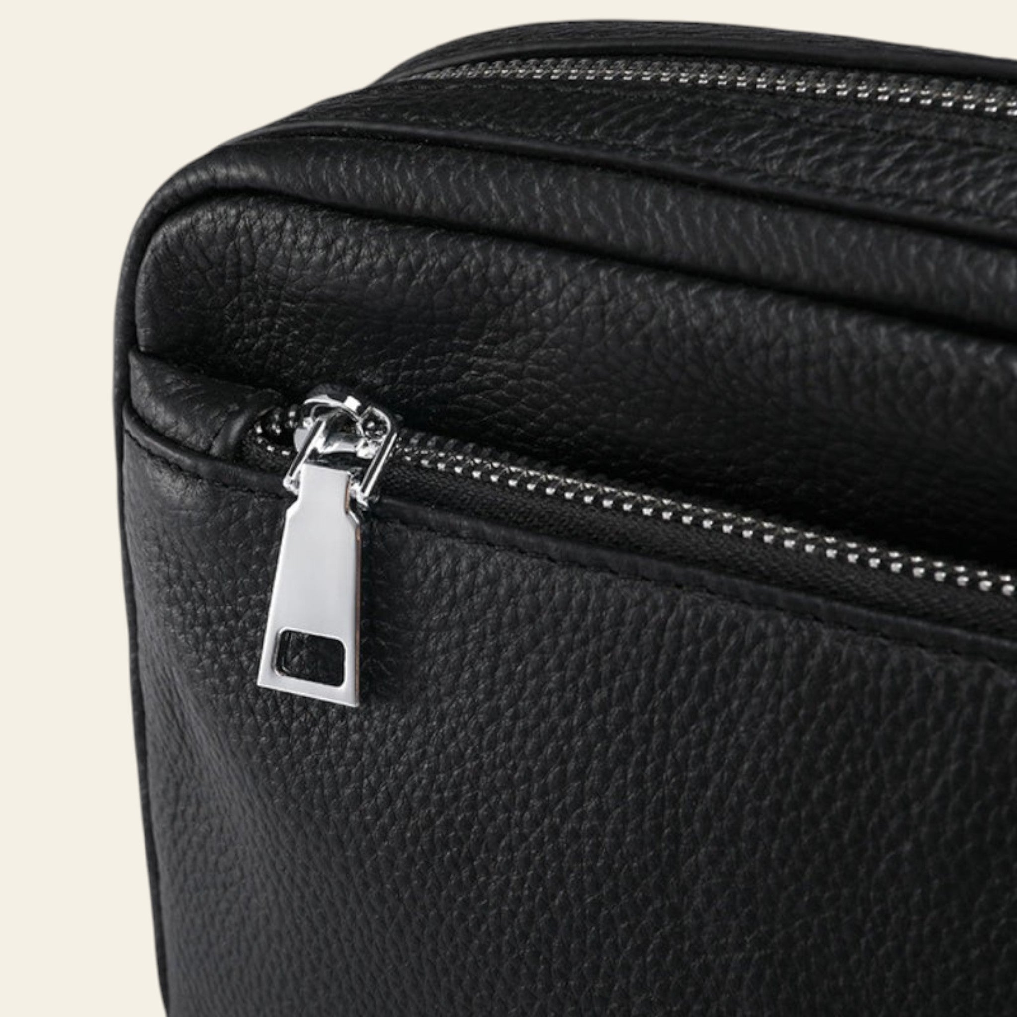 Close-up of a black leather bag with a silver zipper on a white background