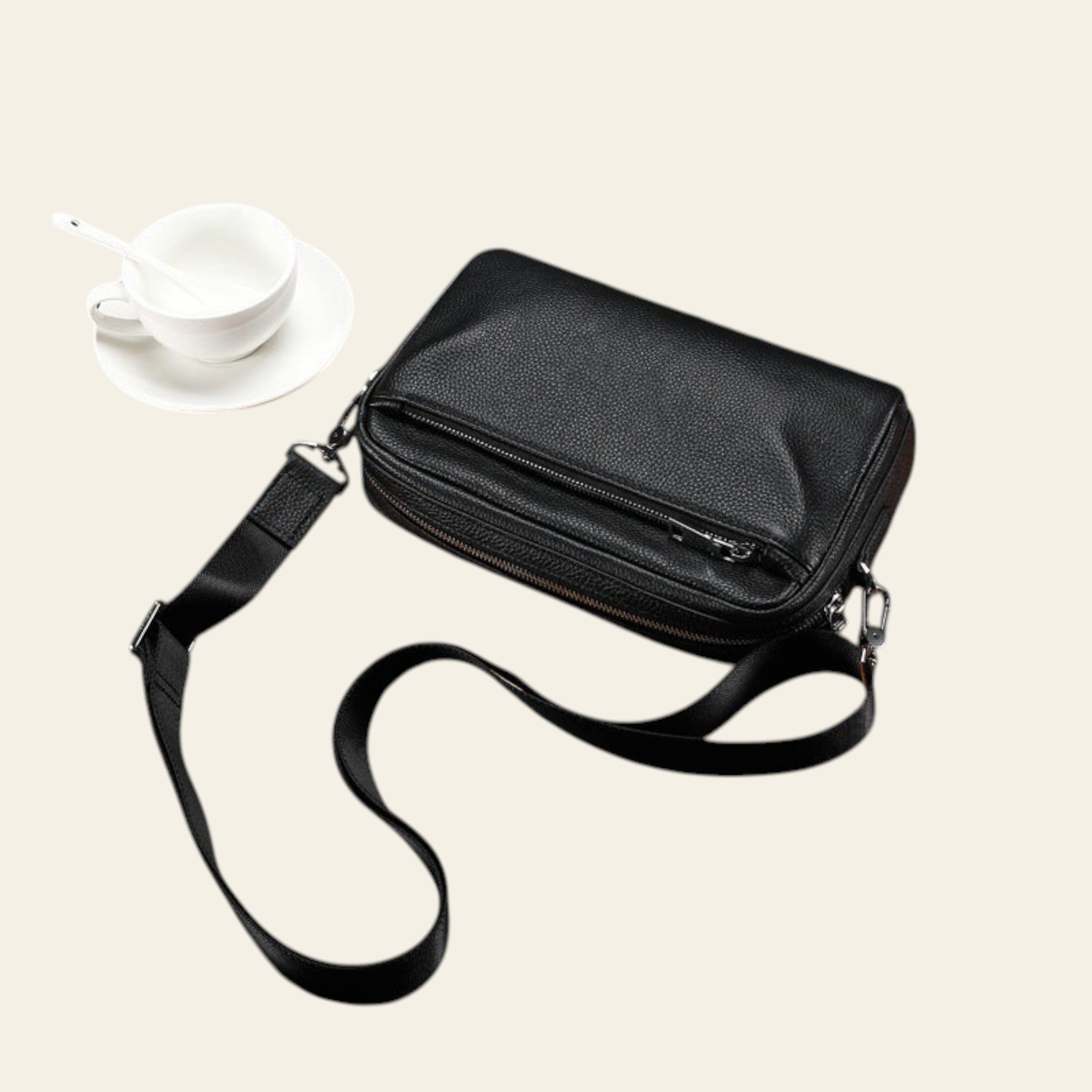 Black crossbody bag on a wooden tray with a cup of tea in the background
