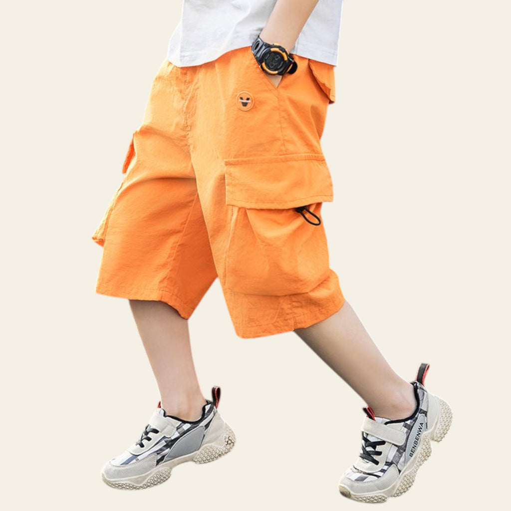 Person wearing bright orange shorts and white sneakers on a street.